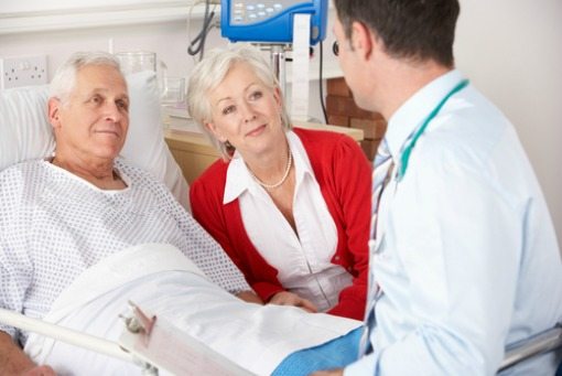 doctor visiting elderly man in his hospital room and his wife