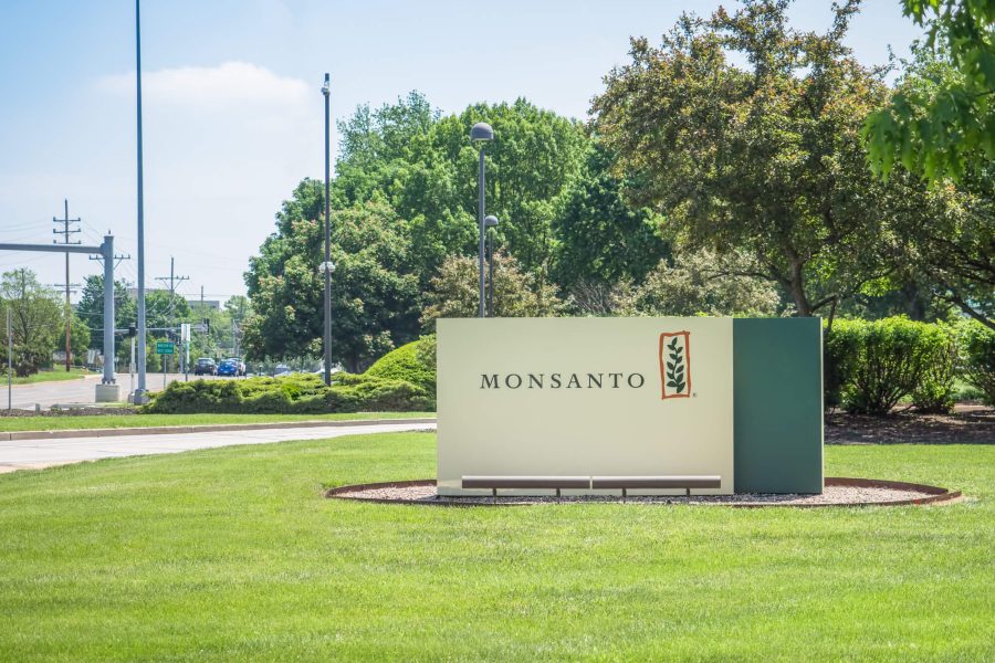 Monsanto corporate headquarters entrance sign, surrounded by green lawn with treeline on the background on a clear day.
