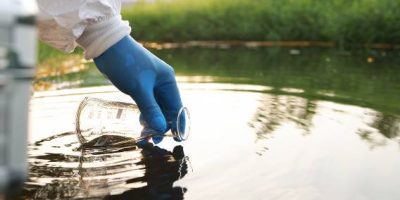 Gloved hand gathering water in beaker