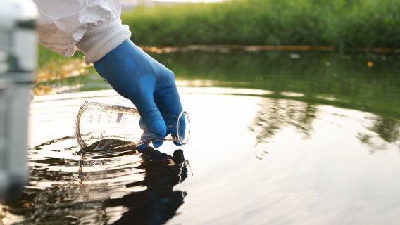 Gloved hand gathering water in beaker