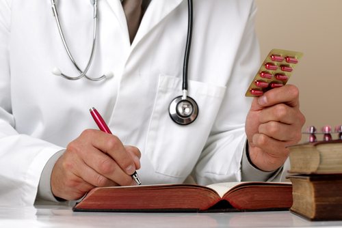 Doctor holding up pills and writing in a book Doctor holding up pills and writing in a book