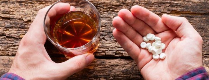 person holding alcohol and pills